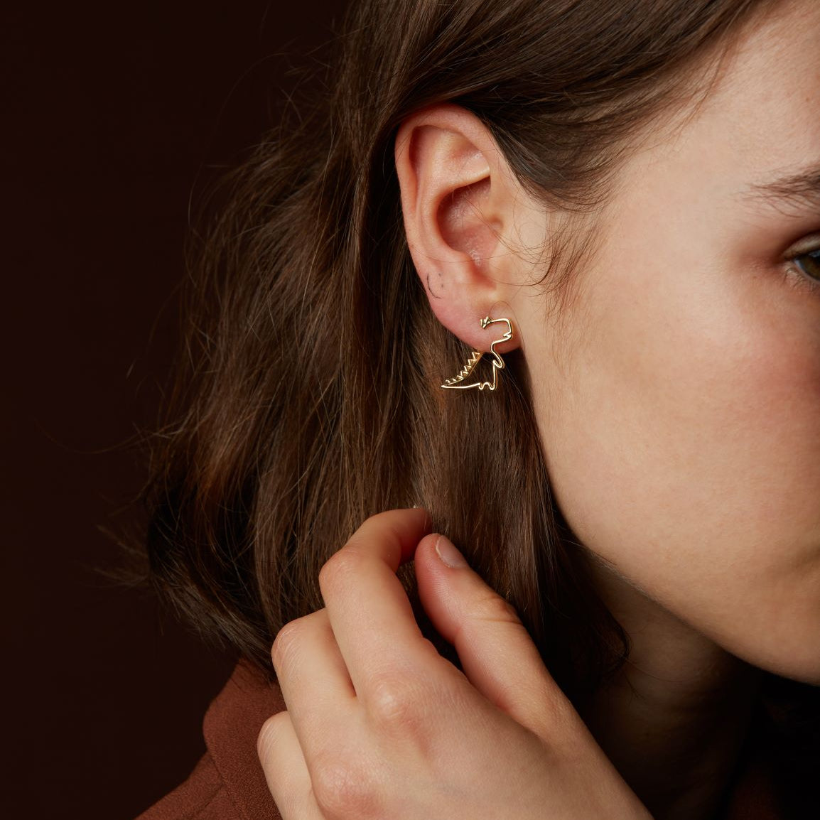Gold dinosaur shaped earring worn by model
