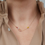Gold chain necklace with gold tennis racquet and ball shaped pendants in pink and yellow enamel worn by model