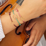 Pink cord bracelet with gold seated cat shaped pendant worn by model holding violin